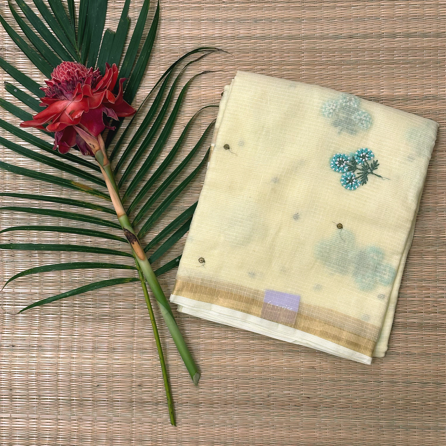 Folded fabric with floral patterns next to a red flower and green leaf on a wooden surface